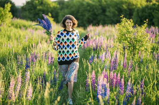 Smiling woman walks through a summer field holding lupine flowers