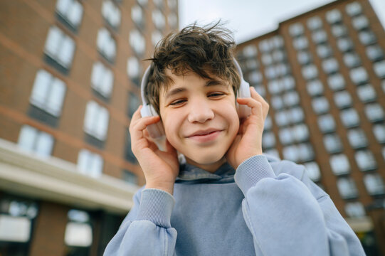 A smiling teenager listens to music with a headphone in the city