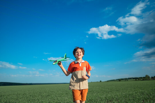 Happy boy runs in a summer field launching a toy airplane