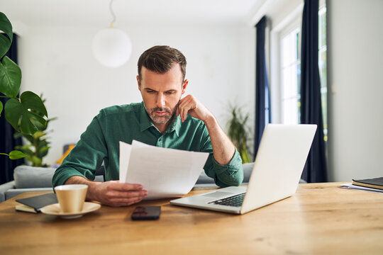 Worried businessman doing paperwork sitting at table working from home