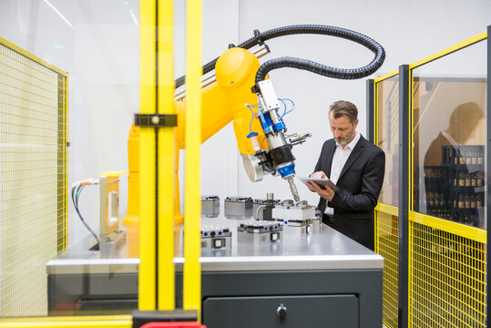 Mature businessman controlling industrial robots with digital tablet