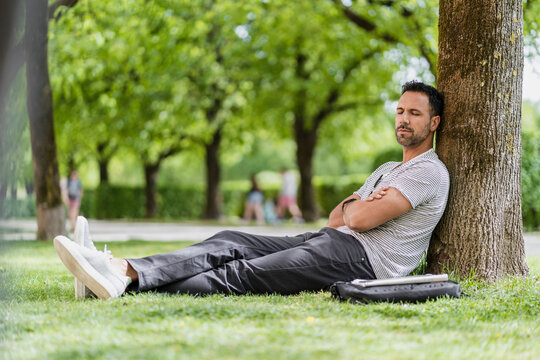 Man leaning against a tree in park having a nap