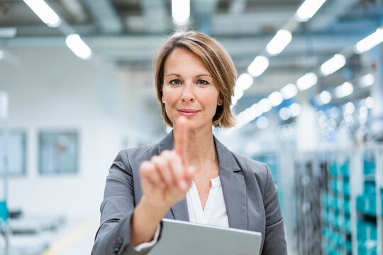 Portrait of businesswoman with tablet in a modern factory touching virtual screen