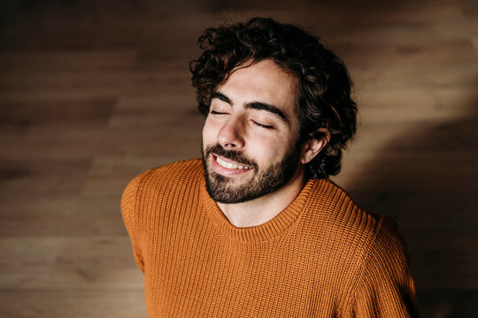 Smiling young man sitting on hardwood floor with eyes closed