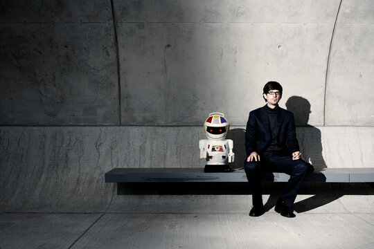 Businessman sitting on a concrete bench next to a toy robot