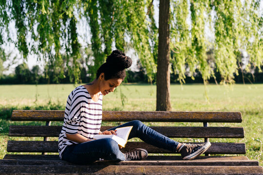 Young woman sitting on park bench reading a book