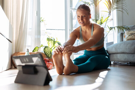 Woman with digital tablet stretching while exercising at home