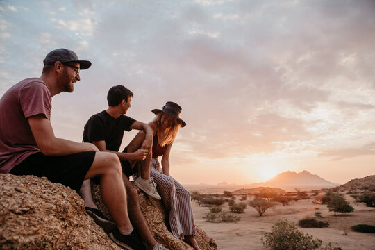 Namibia, Spitzkoppe, friends sitting on a rock at sunset