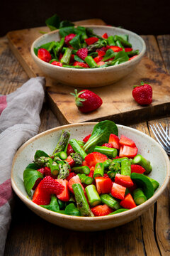 Two bowls feature fresh strawberry and green asparagus salad on wood