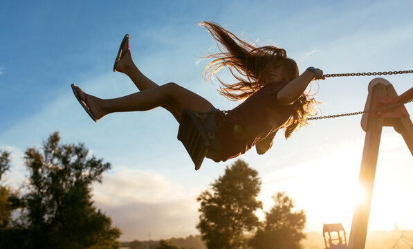 Girl with blowing hair on a swing at backlight