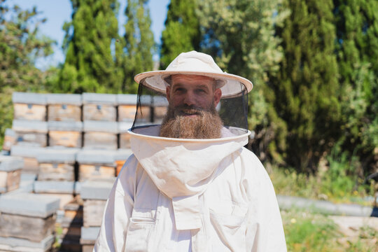 Male beekeeper in protective suit standing at an outdoor apiary