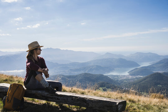Contemplative woman wearing hat and sunglasses sitting on bench