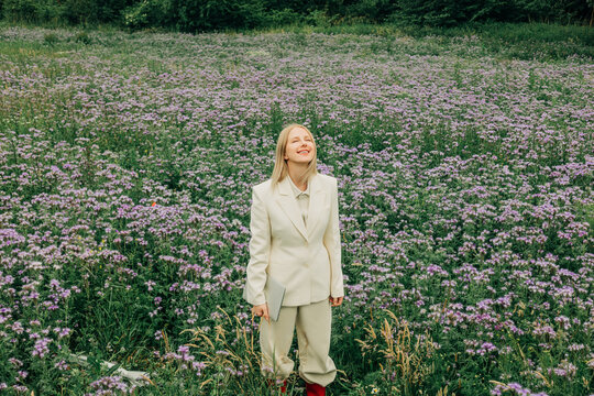 A relaxed businesswoman in a suit holds a laptop in a summer meadow