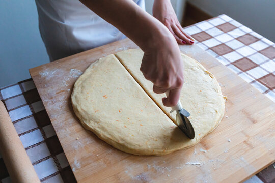 Woman cutting dough with pizza cutter to make croissants in kitchen
