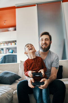 Father and son sitting together on the couch playing computer game