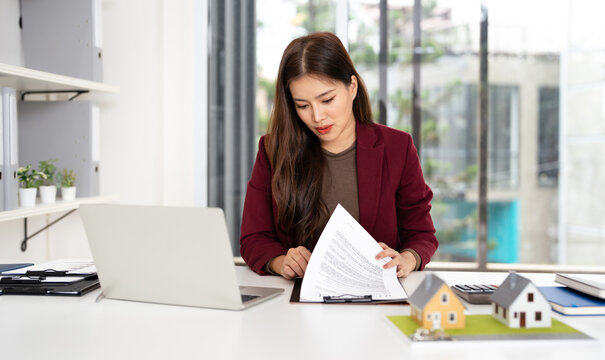 real estate agent professional reviewing documents while working on a laptop.