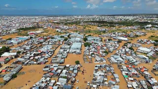 Devastating wide angle aerial view of a massive makeshift refugee camp city in Somalia showing rows of metal sheet tents and dirt roads representing global migration