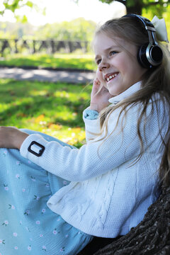Smiling Girl Enjoying Music Outdoors with Headphones in a Sunny Park