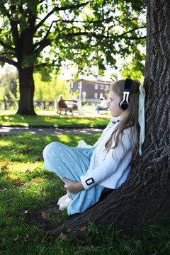 Young Girl Listening to Music Under a Tree in Autumn Park