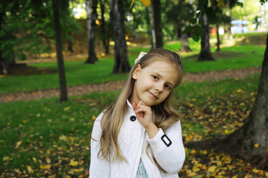 Smiling Girl in White Sweater Posing Amidst Autumn Trees in Park Setting