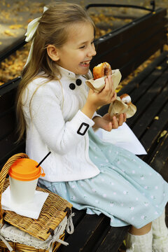 Cheerful Girl Enjoying Pastry on Park Bench During Autumn Outing with Picnic Basket