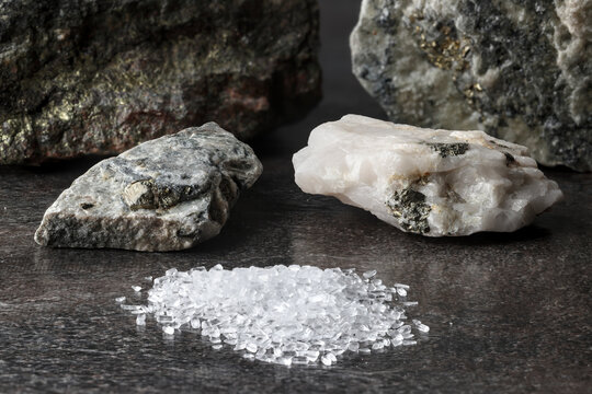 Mineral ore in background. Magnesium sulphate, MgSO₄, Epsom salt in foreground. Use in industry and mining, e.g., lixiviant in extraction of rare earths from ion-adsorption clay deposits