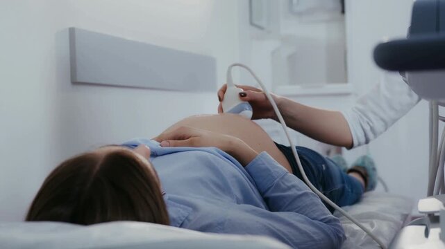 Pregnant woman receiving ultrasound examination while lying comfortably in clinic bed