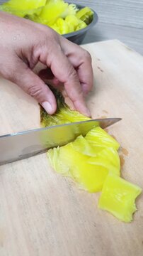 Slicing pickled mustard greens on a wooden cutting board with a knife. Prepping traditional Asian ingredients for cooking a savory homemade recipe