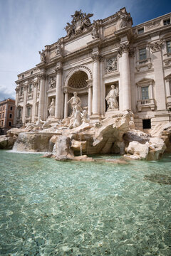 The majestic Trevi Fountain with crystal clear turquoise water in the foreground under sunny sky in Rome, Italy