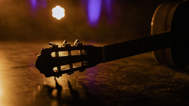 Nylon string guitar resting on stage floor with colorful blurred lights