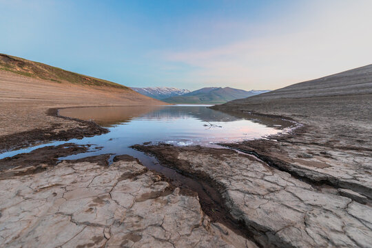 Narrow river winding through dry arid landscape, creating a striking contrast between flowing water and barren terrain, showcasing resilience, natural beauty, and environmental diversity.