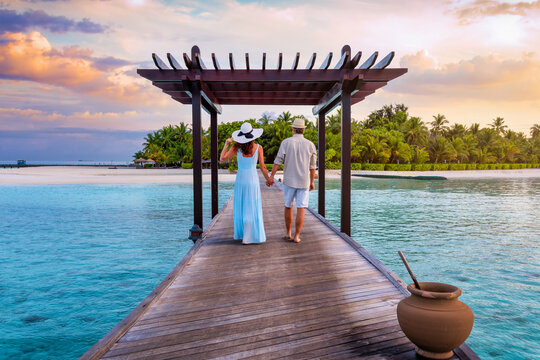 A couple on a romantic vacation walks down a pier in the tropical Maldives islands during sunset time