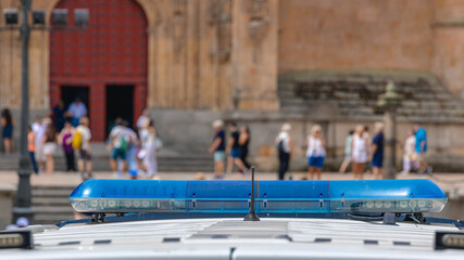 Obraz premium Police patrol car blue emergency light bar in front of blurred tourists near a historic building