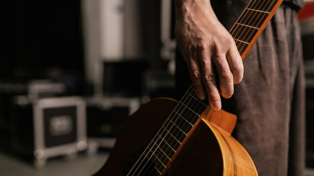 Musician carrying acoustic guitar backstage near equipment cases before live show
