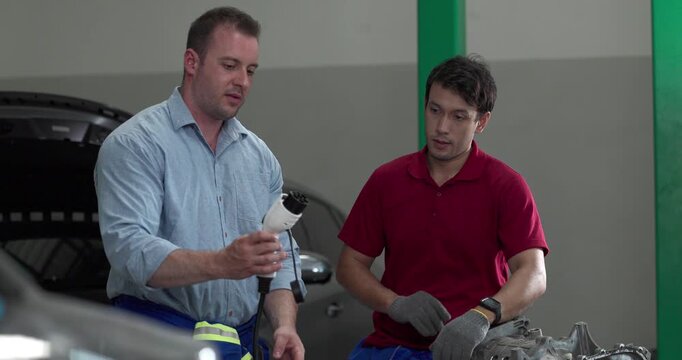 Senior engineer and technician inspecting electric vehicle motor component with high voltage cable