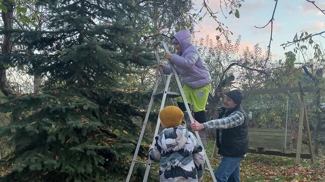 Young dad with daughter and son of primary school age in warm autumn clothes enjoying quality time together in the yard among fallen golden leaves. Cozy family autumn concept. The beauty of fall .
