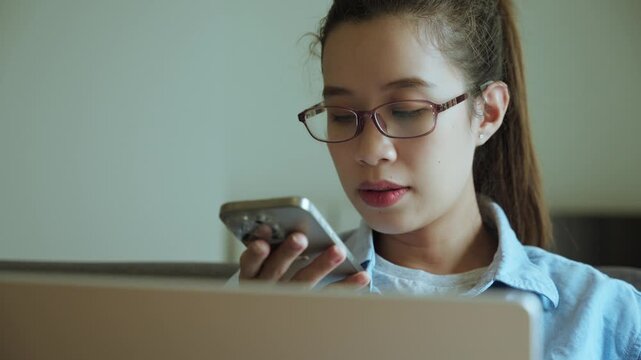 Young Asian Woman Using Smartphone Voice Assistant While Sitting on Sofa at Home