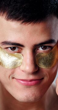 Studio, face and man with eye patches for skincare beauty, grooming cosmetics or facial hydration. Portrait, male person or anti aging treatment with smile or gold mask for collagen or dermatology