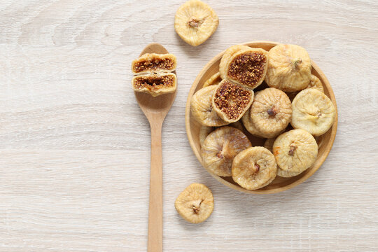 Dried figs in a wooden bowl and on a wooden spoon, healthy dried fruit snack, top view, isolated on a light wood background.