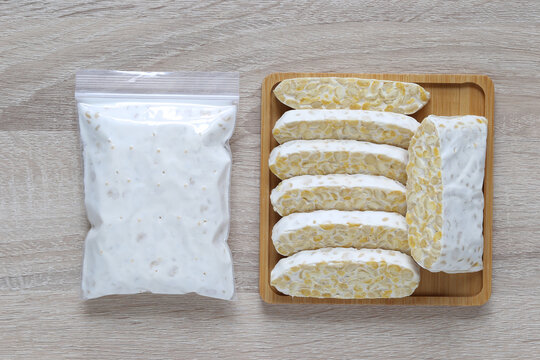 Fresh raw tempeh slices on a wooden tray with a sealed plastic bag, healthy plant-based fermented soybean food ingredient.