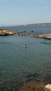 Aerial view of a woman on a stand up paddleboard in the pristine turquoise waters of a rocky cove on tabarca island, with the spanish coastline visible in the sunny background