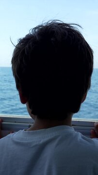 Back view of a silhouetted kid enjoying a ferry trip to tabarca island, admiring the beautiful seascape through the window as his hair blows gently in the ocean breeze during summer days
