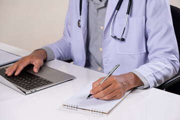 Fototapeta premium Doctor Using Laptop While Writing Medical Notes in Clinic Office