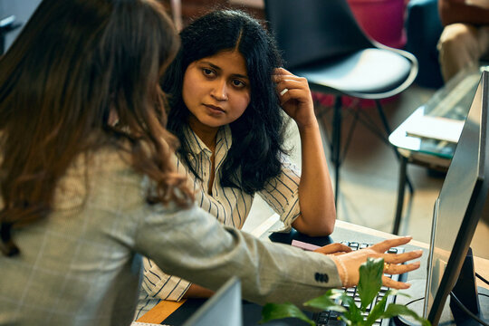Female colleagues reviewing computer screen during one to one workplace consultation. Concept of digital onboarding, practical training, software guidance, knowledge transfer, and employee support.
