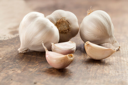 Rustic composition of fresh whole garlic bulbs and scattered cloves on a wooden kitchen table, healthy cooking and culinary concept.