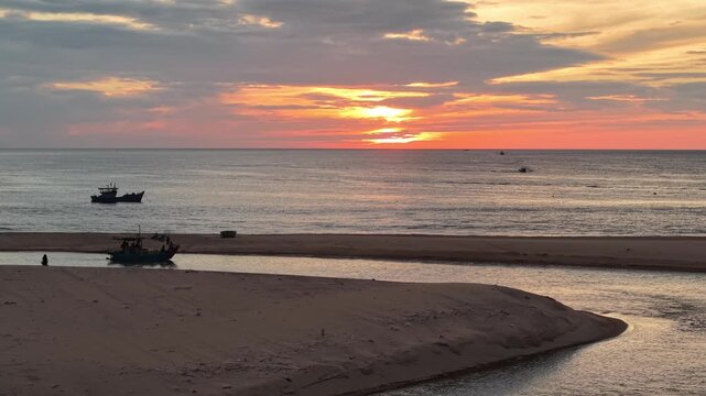 Drone captures the confluence where a river empties into the ocean, with a sandbar separating the waters and fishing boats scattered across the estuary at dawn.