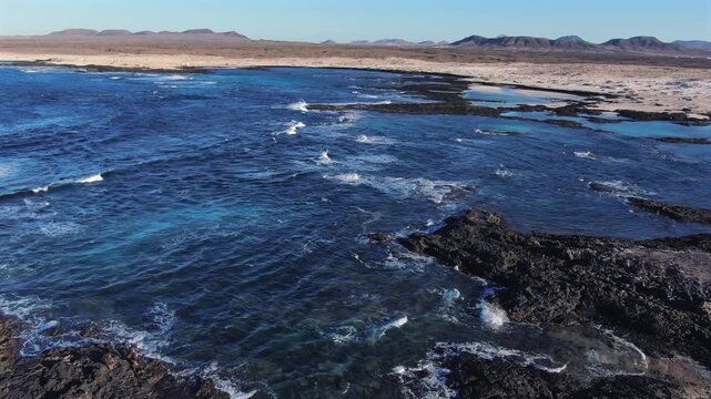Aerial view of volcanic coastline with waves breaking on black lava rocks near El Cotillo in Fuerteventura, Canary Islands