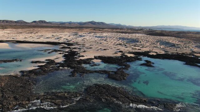 Stunning aerial footage showing the turquoise water, white sand, and black volcanic rocks near the Toston Lighthouse in Fuerteventura