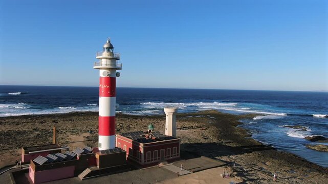 Aerial view of the Toston Lighthouse on the Fuerteventura coast with a clear blue sky and ocean waves crashing on the shore