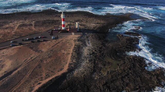 High angle perspective of the Toston lighthouse in El Cotillo, Fuerteventura. The ocean waves are breaking against the rugged volcanic coast